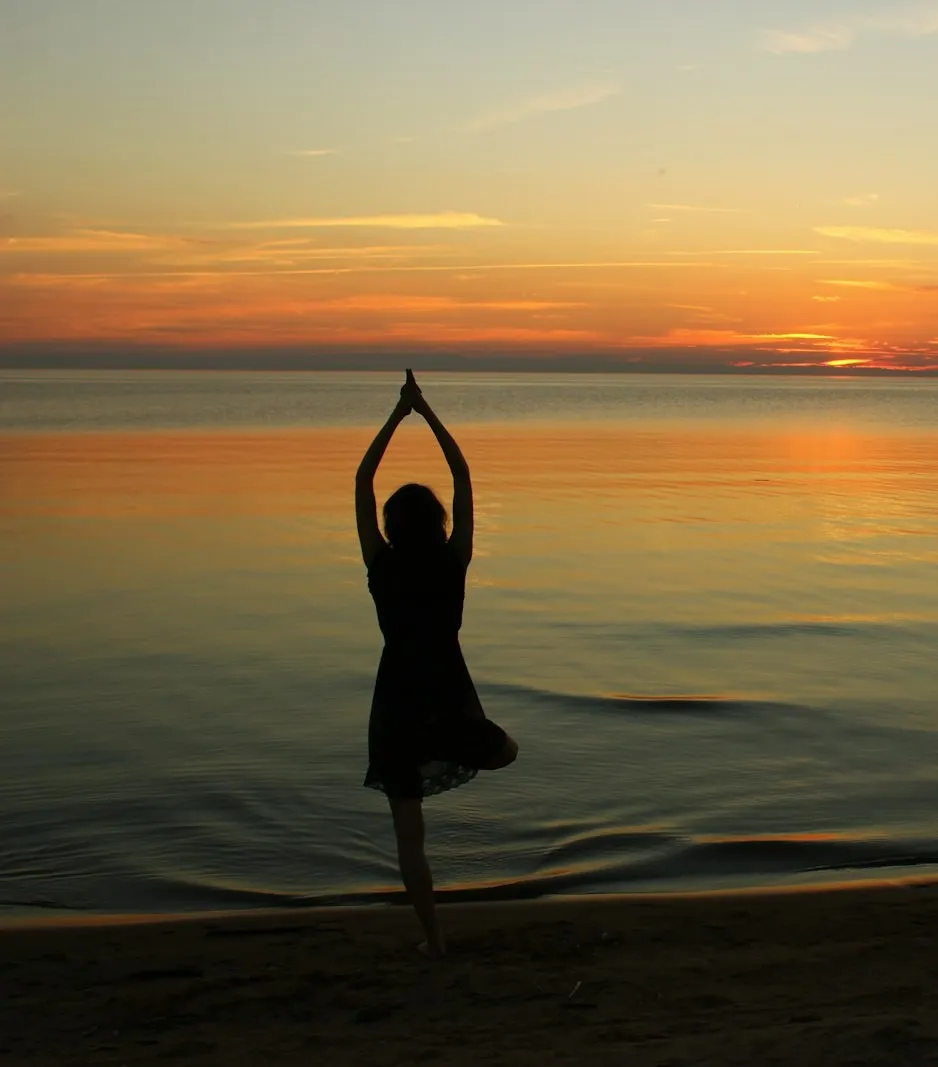 Student practising tree pose on a calm beach at golden hour